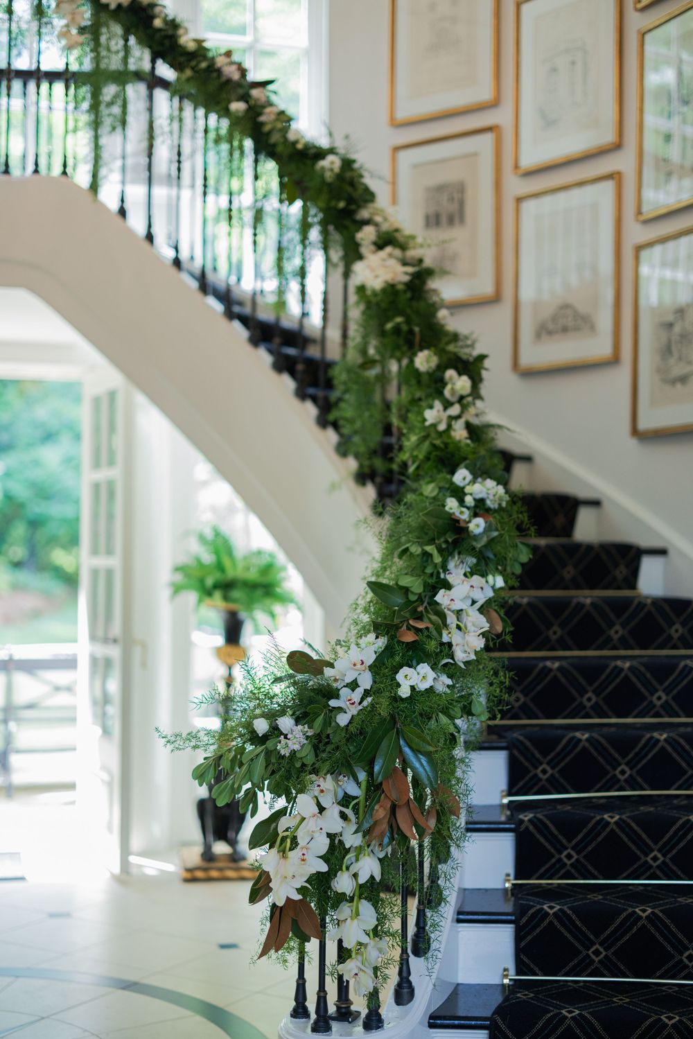 Elegant staircase adorned with lush green and white floral garland draped along black banister for a wedding celebration.