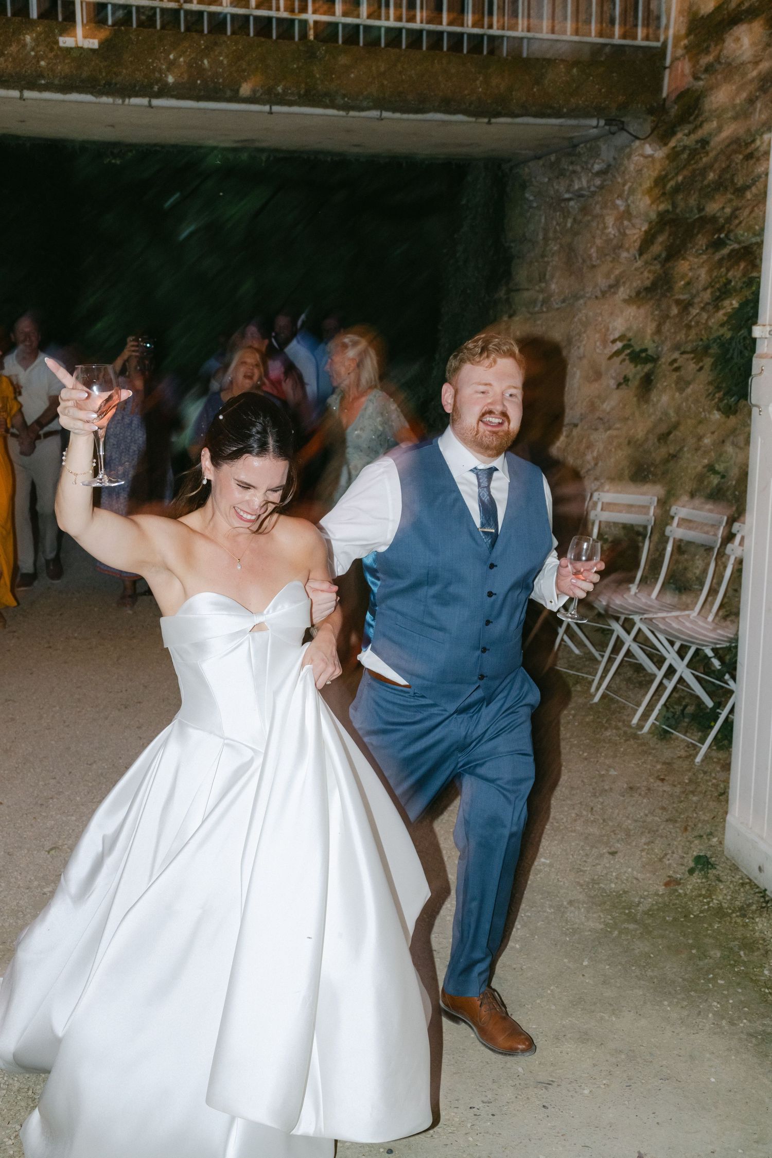 Saxophonist leads wedding procession outdoors at dusk, with bride in white gown and guests following behind.