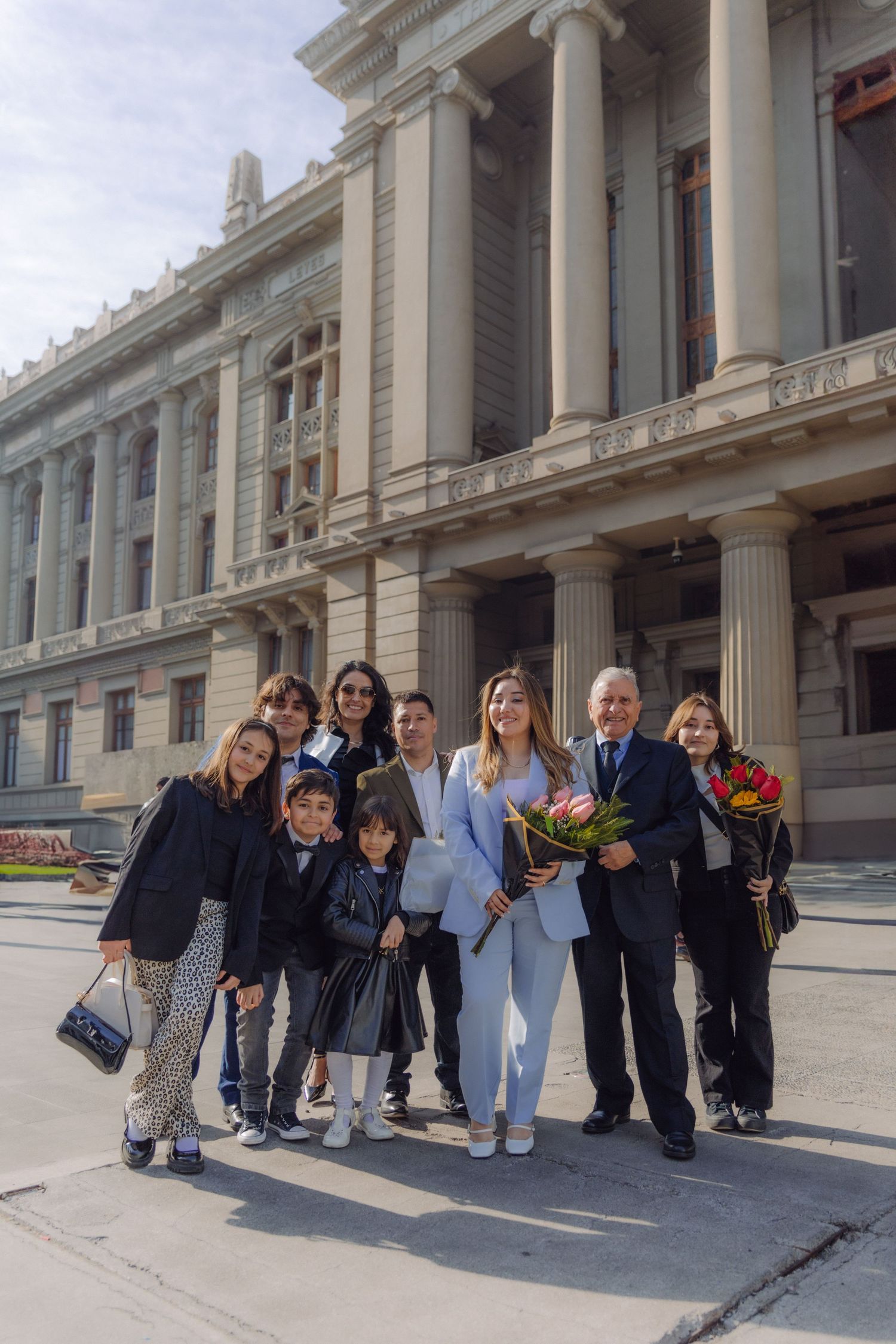 Group family photo with graduate holding flowers outside neoclassical university building.