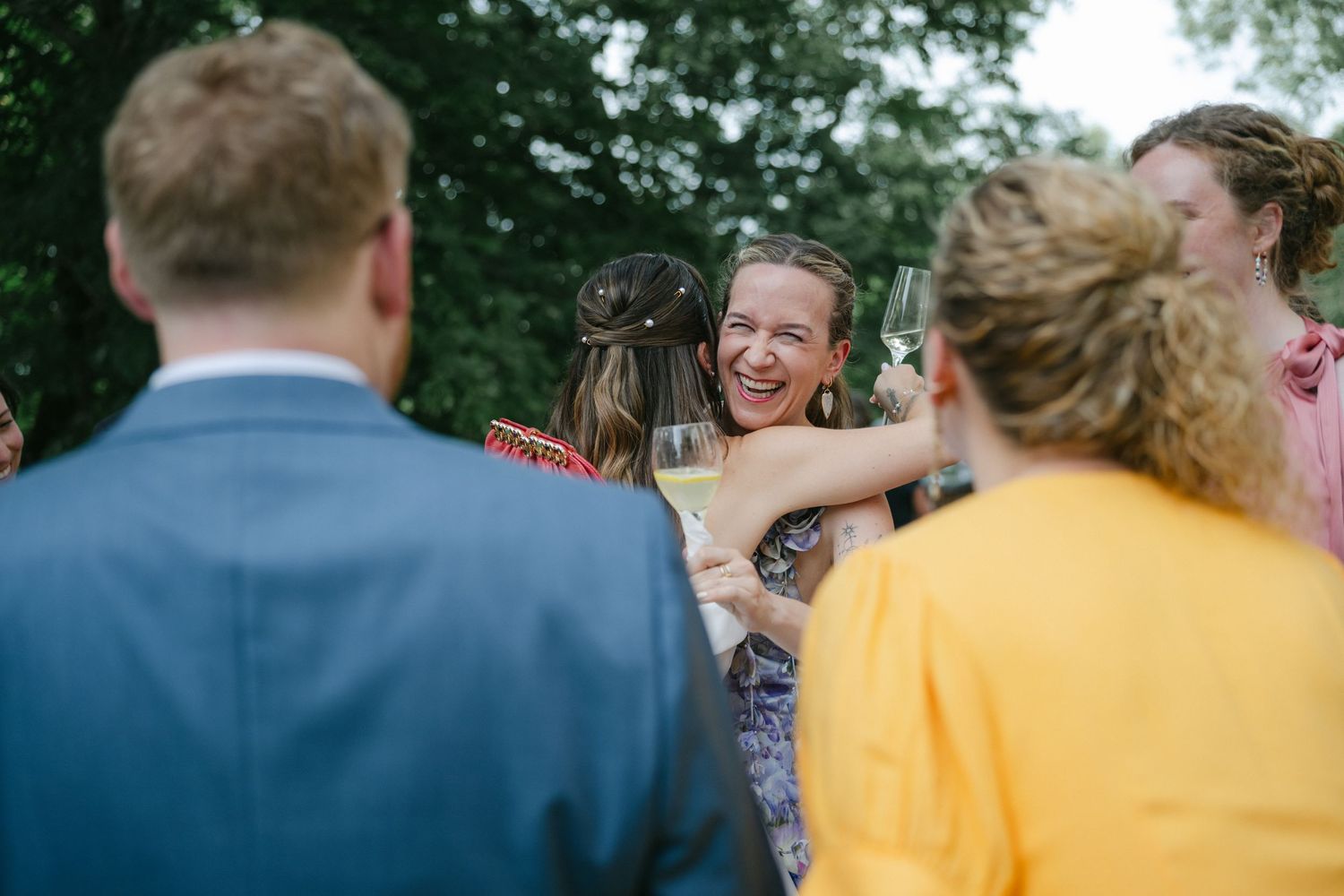 Guests laughing and celebrating outdoors at a wedding reception, woman smiling holding champagne glass.