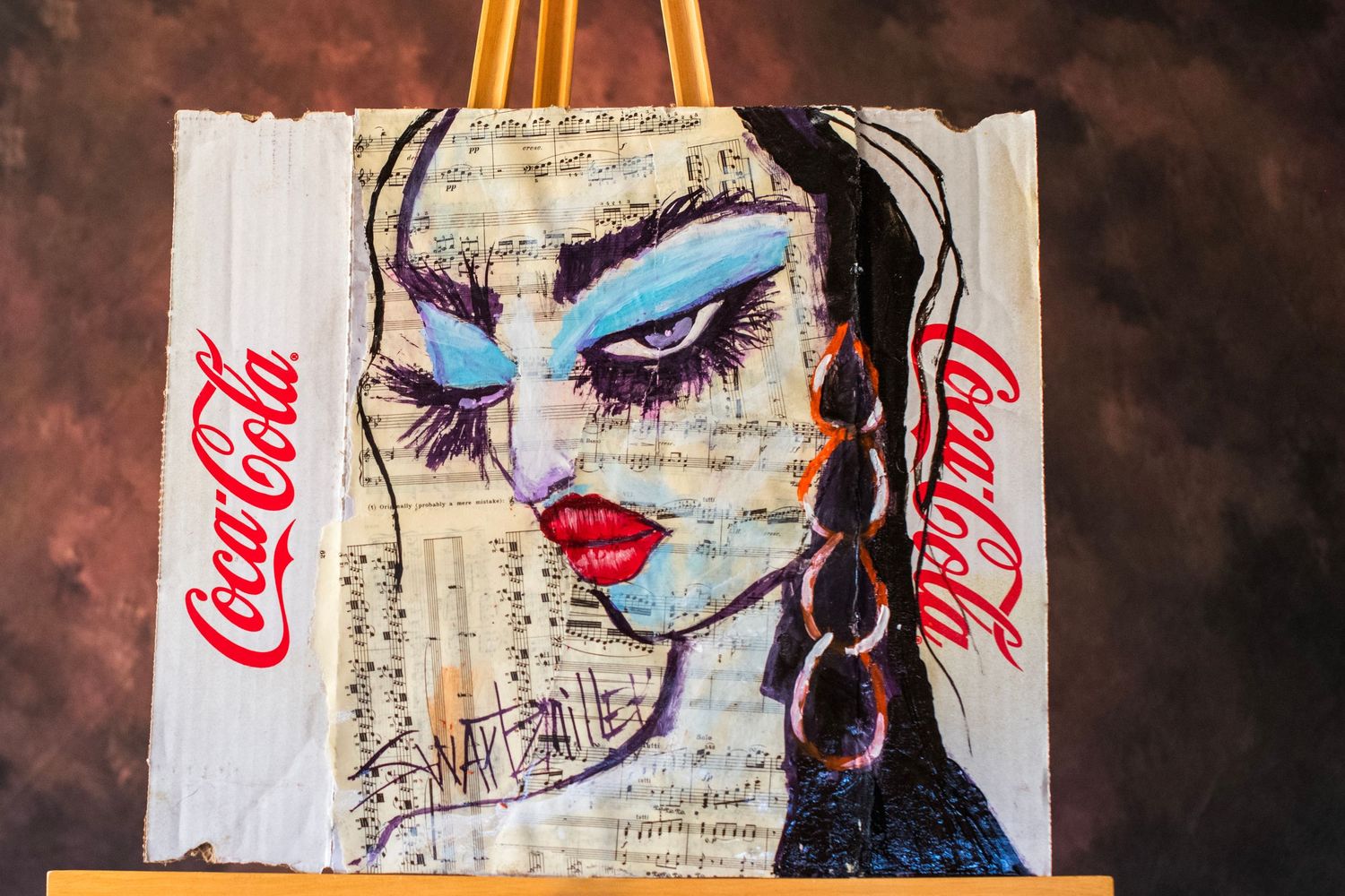 Mixed media painting of a woman with blue eyeshadow on sheet music, framed by Coca-Cola logos on a canvas easel.