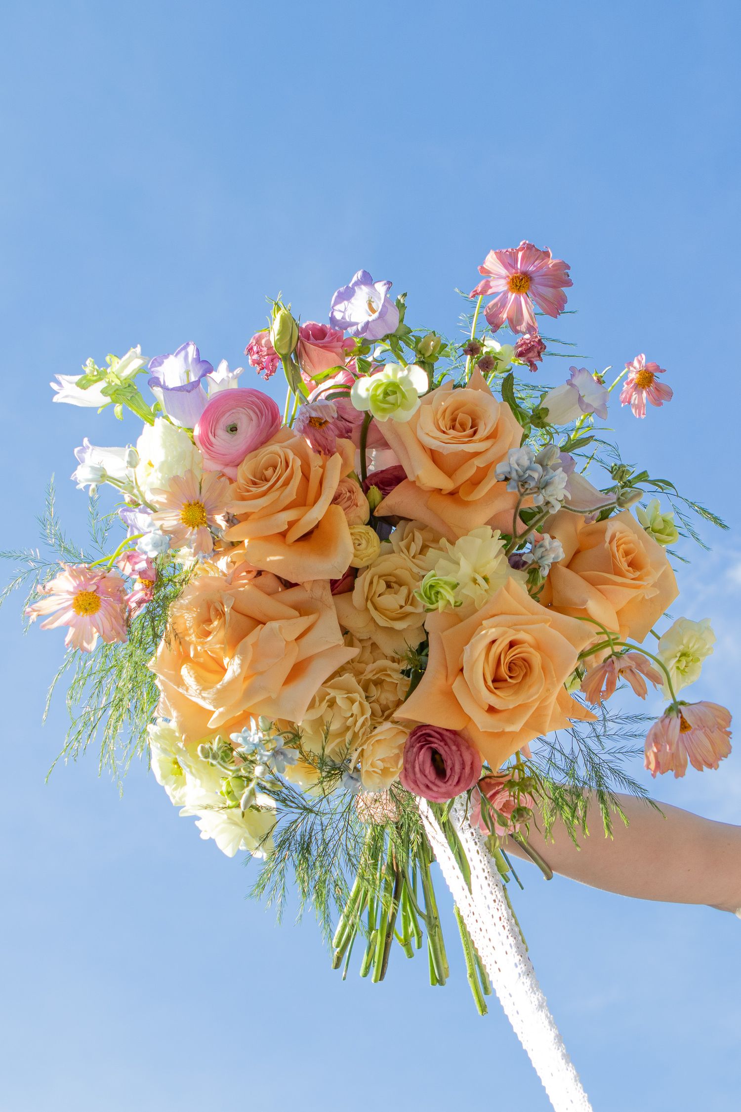 Colorful bridal bouquet thrown into the deep blue sky for wedding photos in strongsville.