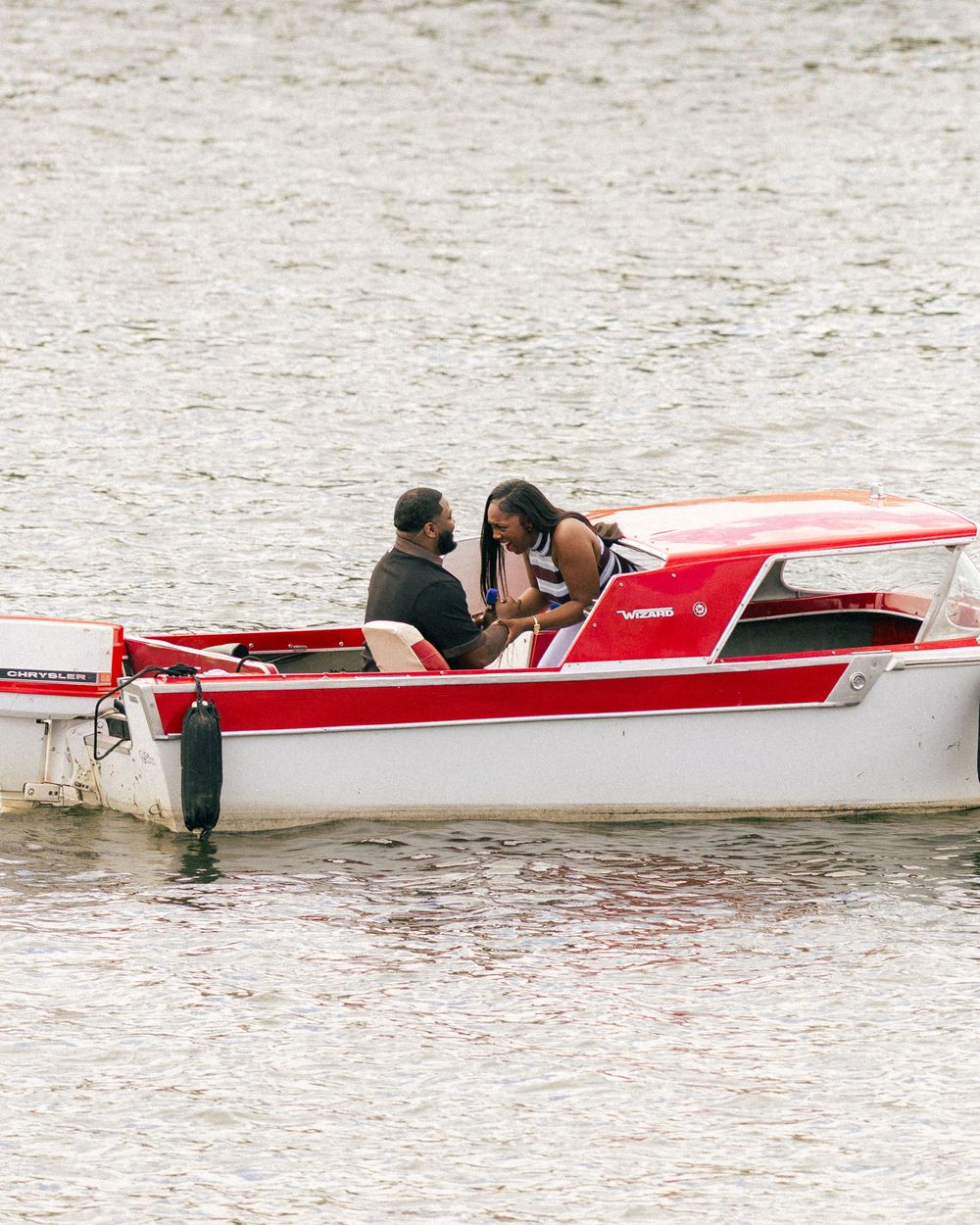 Two people sitting together on a red and white motorboat floating on calm water.