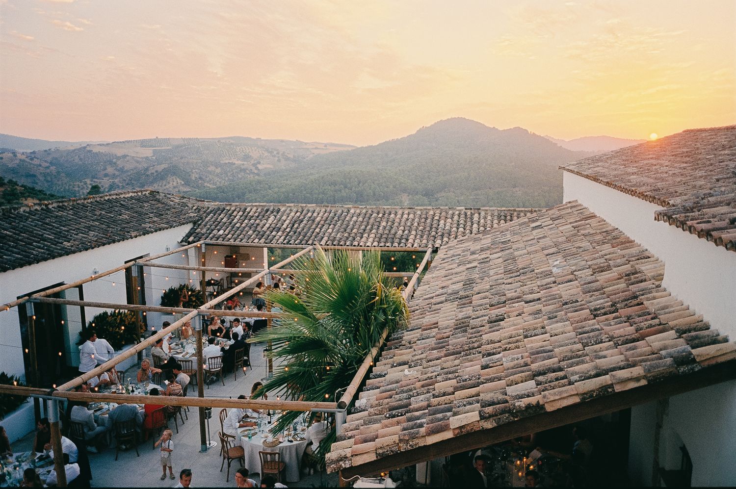 Rustic terracotta rooftop venue with outdoor dining at sunset, overlooking scenic mountain valley landscape.
