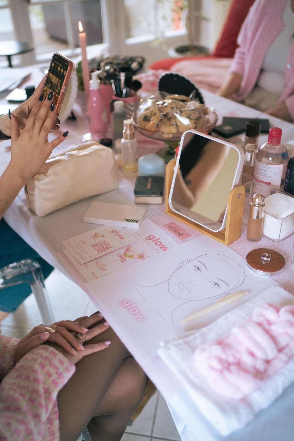 A vanity table with makeup products, a mirror, candle, and a face chart guide with glow markings.