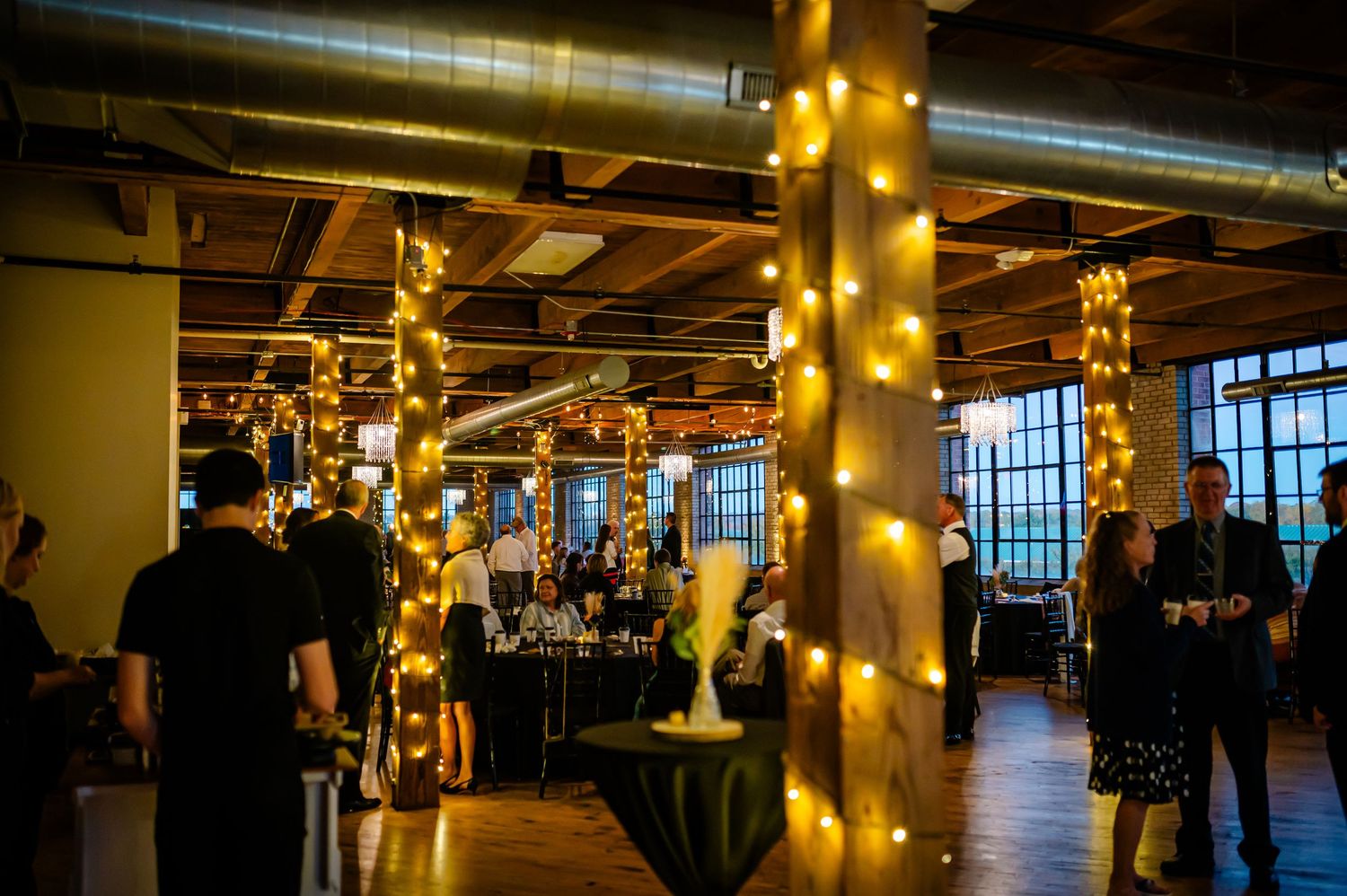 Elegant wedding venue with white chairs, chandelier, brick walls, wood beams, and a floral arch at the altar.