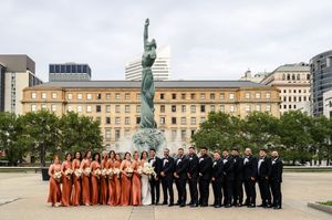 Wedding party poses before a bronze statue in Cleveland's Public Square, bridesmaids in rust gowns and groomsmen in black tuxedos.