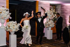 Bride and groom celebrate wedding reception entrance wearing sunglasses, surrounded by white floral arrangements.