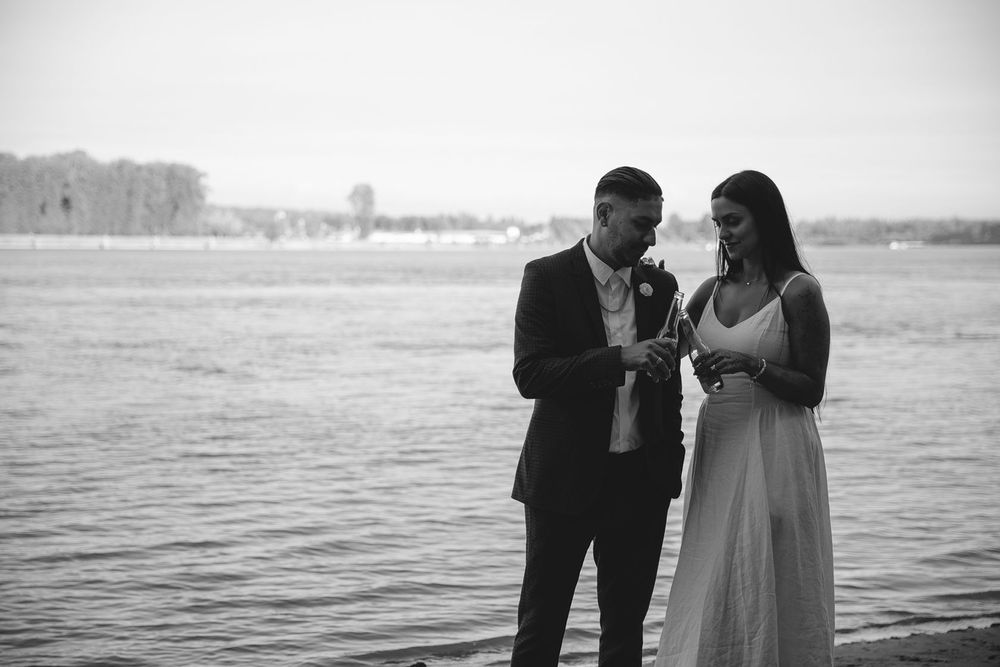 Bride and groom exchange rings by waterside in black and white wedding photo.