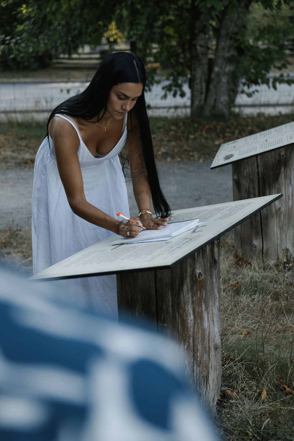Bride in white dress signs wedding ketubah at outdoor wooden stand.