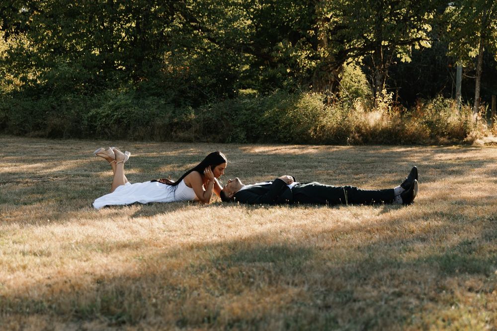 Bride and groom lying in a sunny field during romantic outdoor wedding photo session.