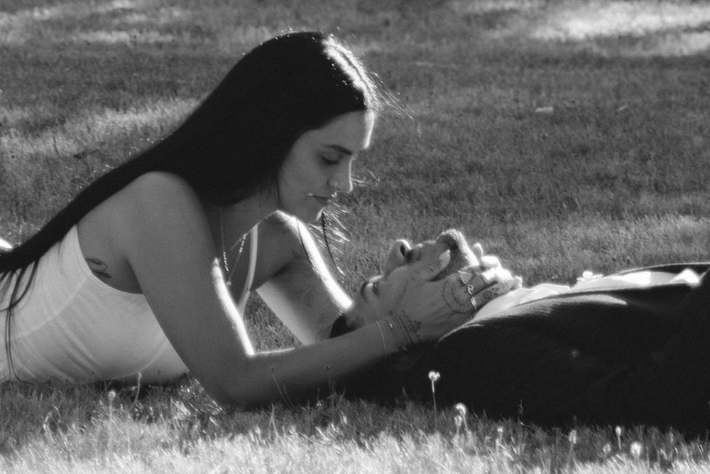 Couple lying on grass facing each other holding hands in a romantic black and white photo.