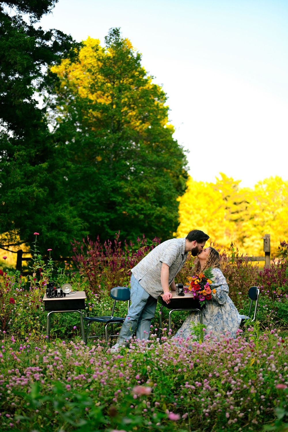 Couple sharing a romantic moment in a wildflower garden with yellow autumn trees in background.