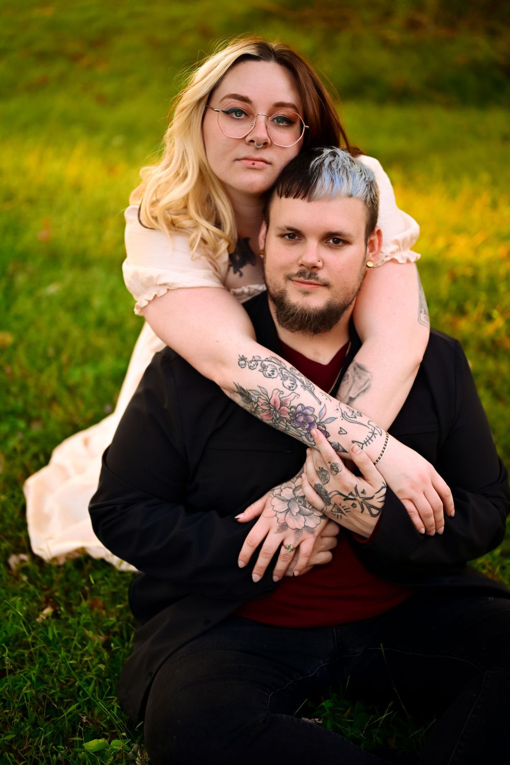 Romantic outdoor portrait featuring couple sitting in green grass during golden hour.