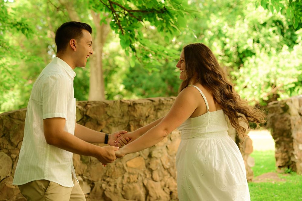 Couple in white outfits dancing together in a romantic garden setting with lush greenery and stone walls.