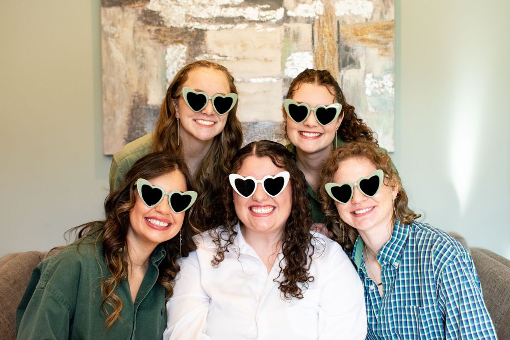 Bride and bridesmaids wearing heart-shaped sunglasses, laughing and posing together during a fun wedding day portrait.
