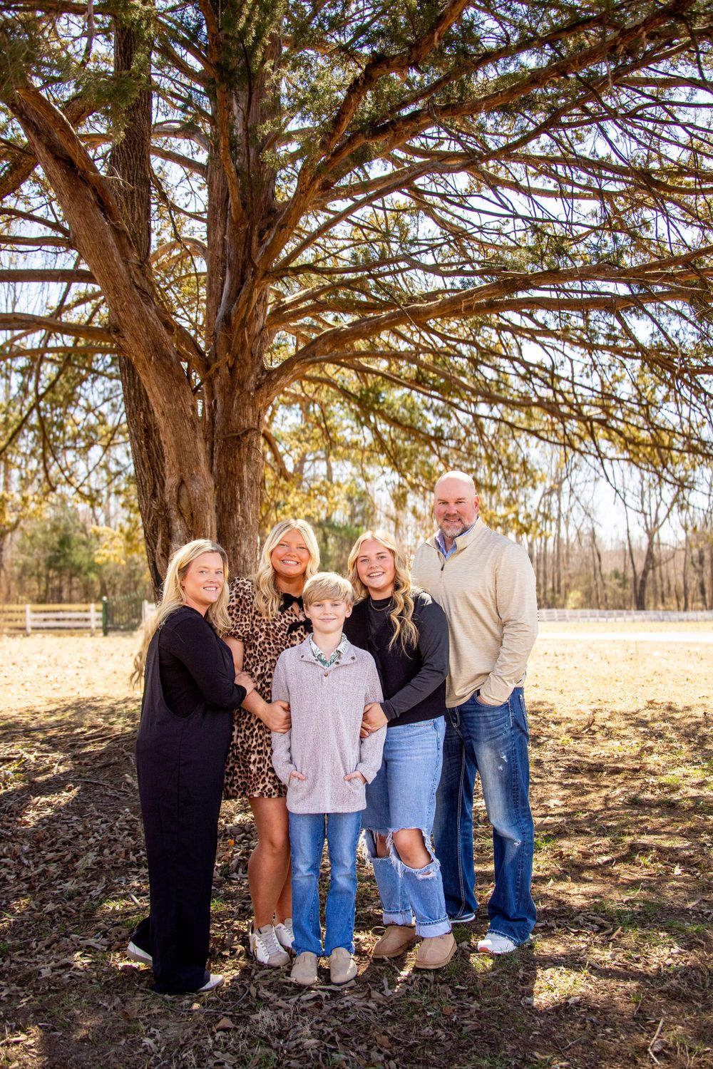 Family standing together in front of a beautiful tree during a fall outdoor portrait session, smiling and enjoying time together.