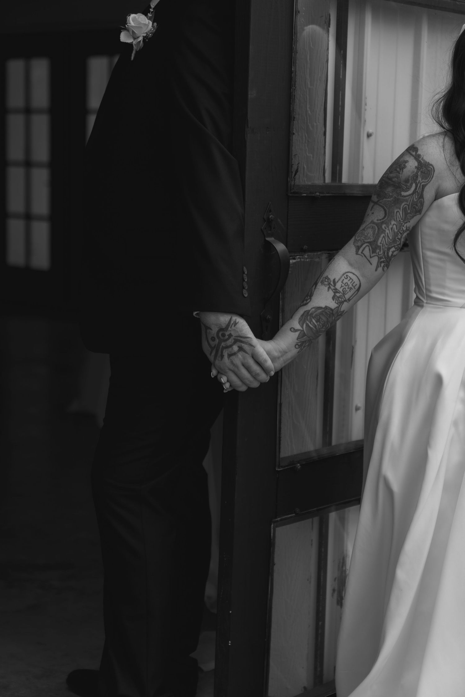 A black and white wedding photo series showing close-up details of a couple holding hands in formal attire.