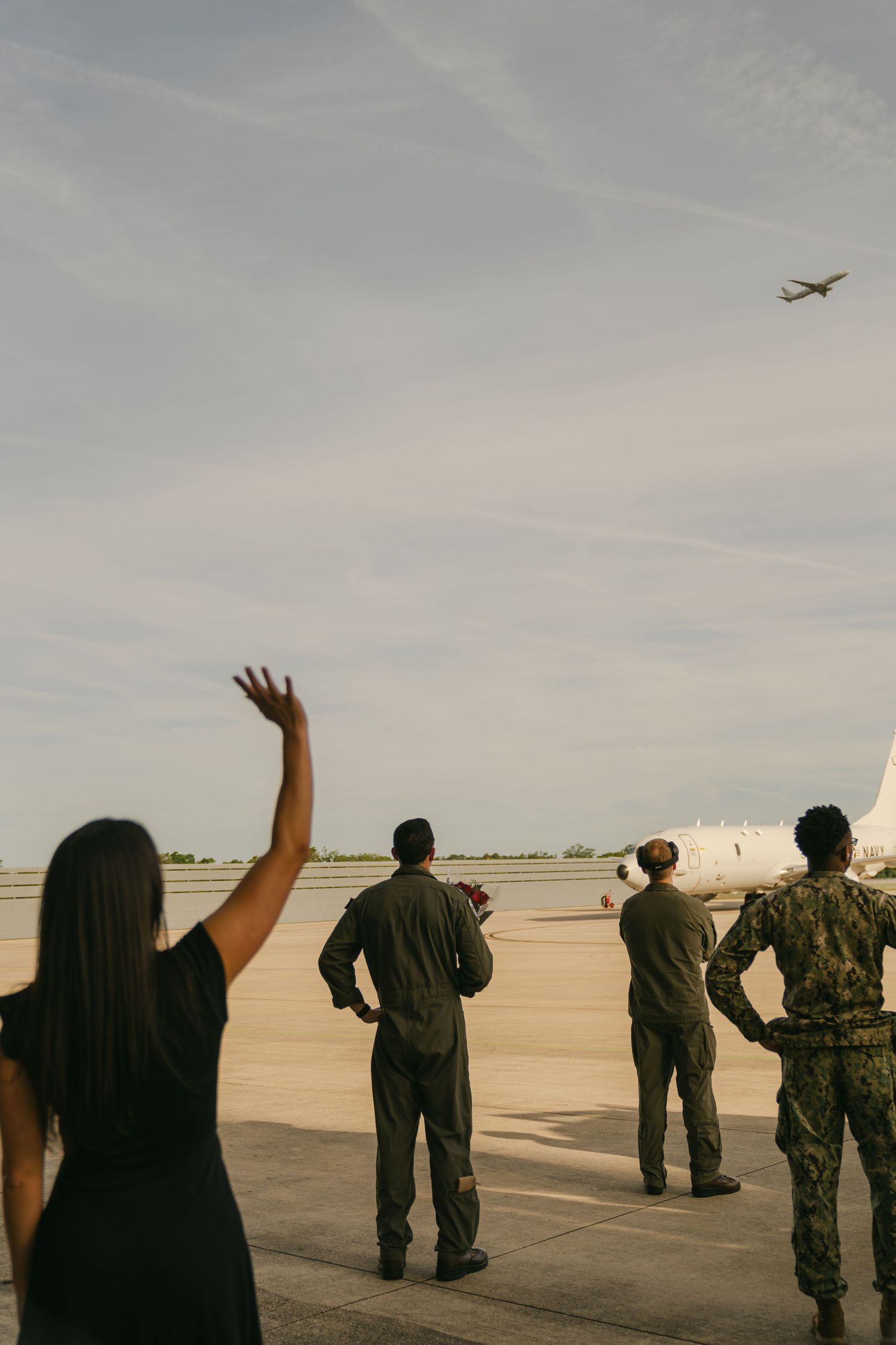 Military personnel waving goodbye on an airfield as plane takes off.