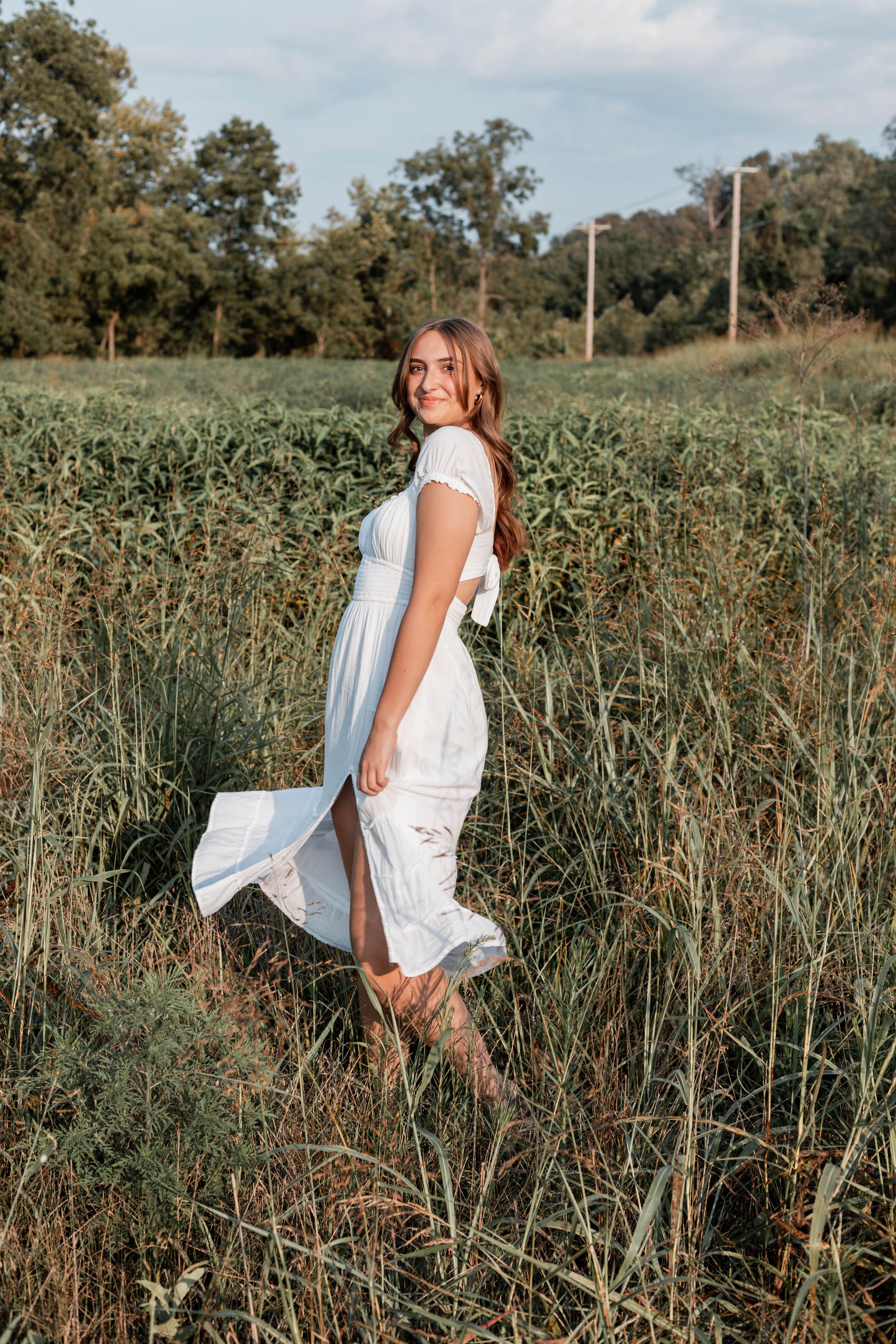 A woman in a flowing white dress twirls in a rustic field during golden hour.