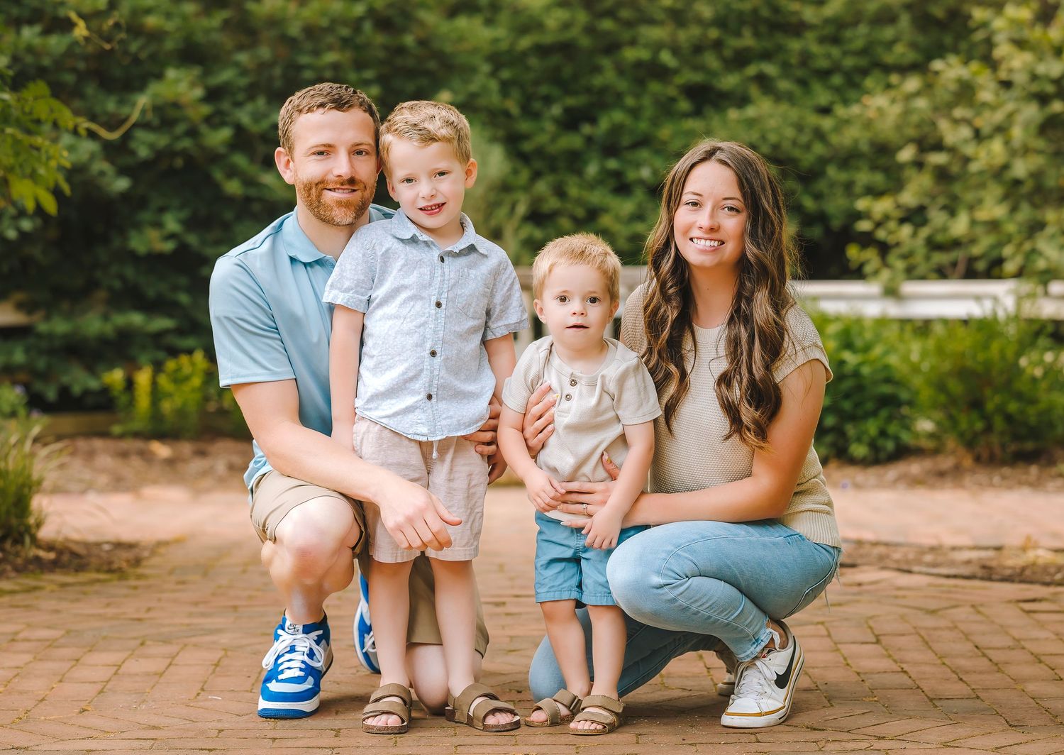 A family of four poses together by a wooden fence at sunset in a park.