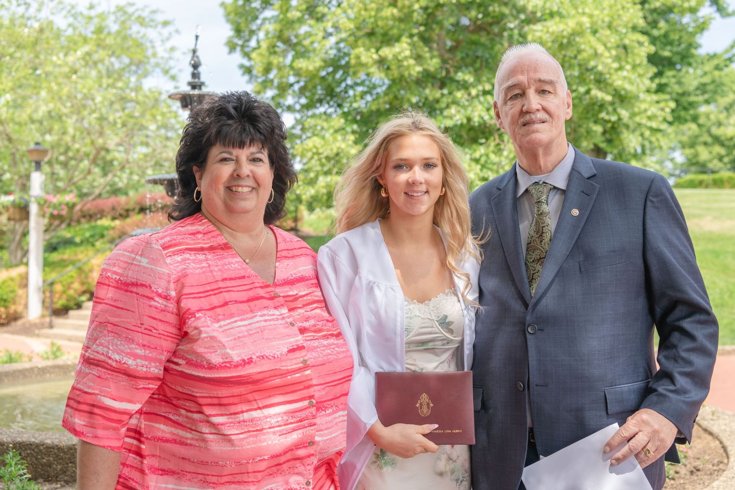 Three people pose together outdoors on a sunny day.