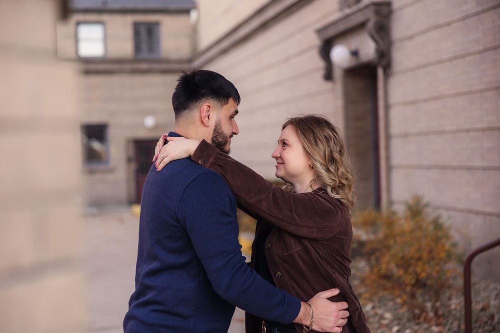A couple embraces tenderly against a beige building exterior.