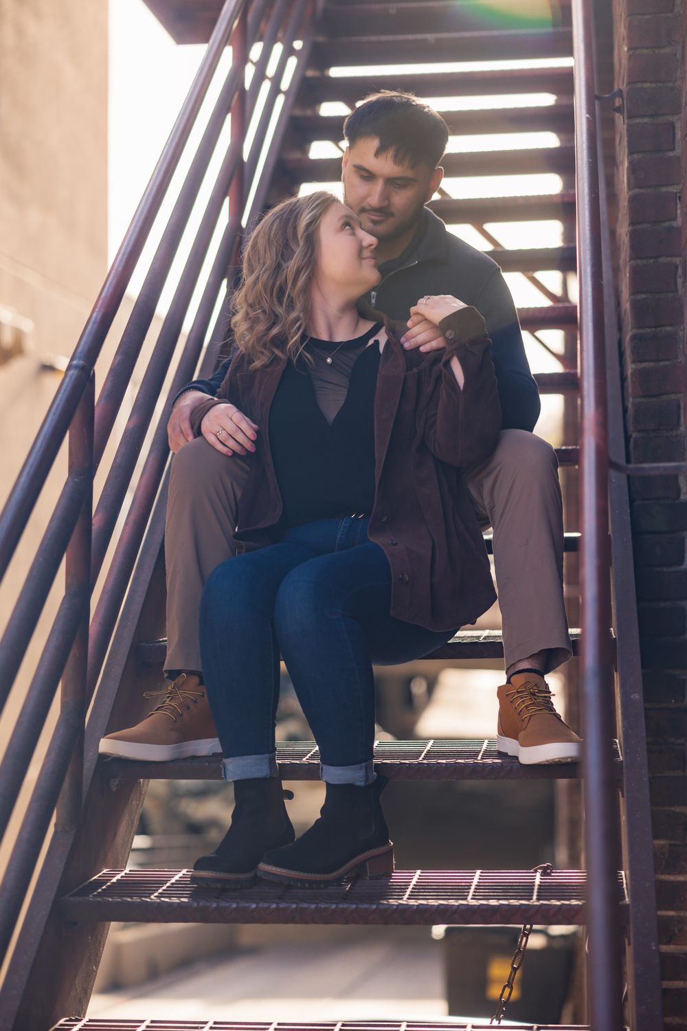 A couple shares a tender moment while sitting on metal stairs outdoors.