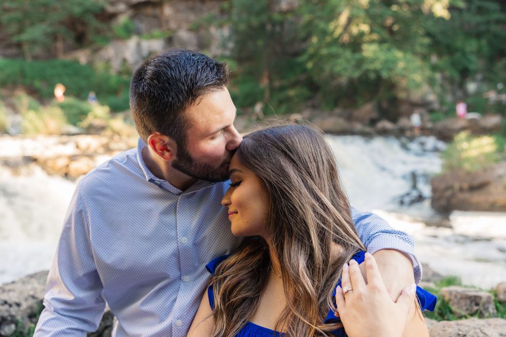 Couple sharing intimate moment outdoors with natural scenery in background.