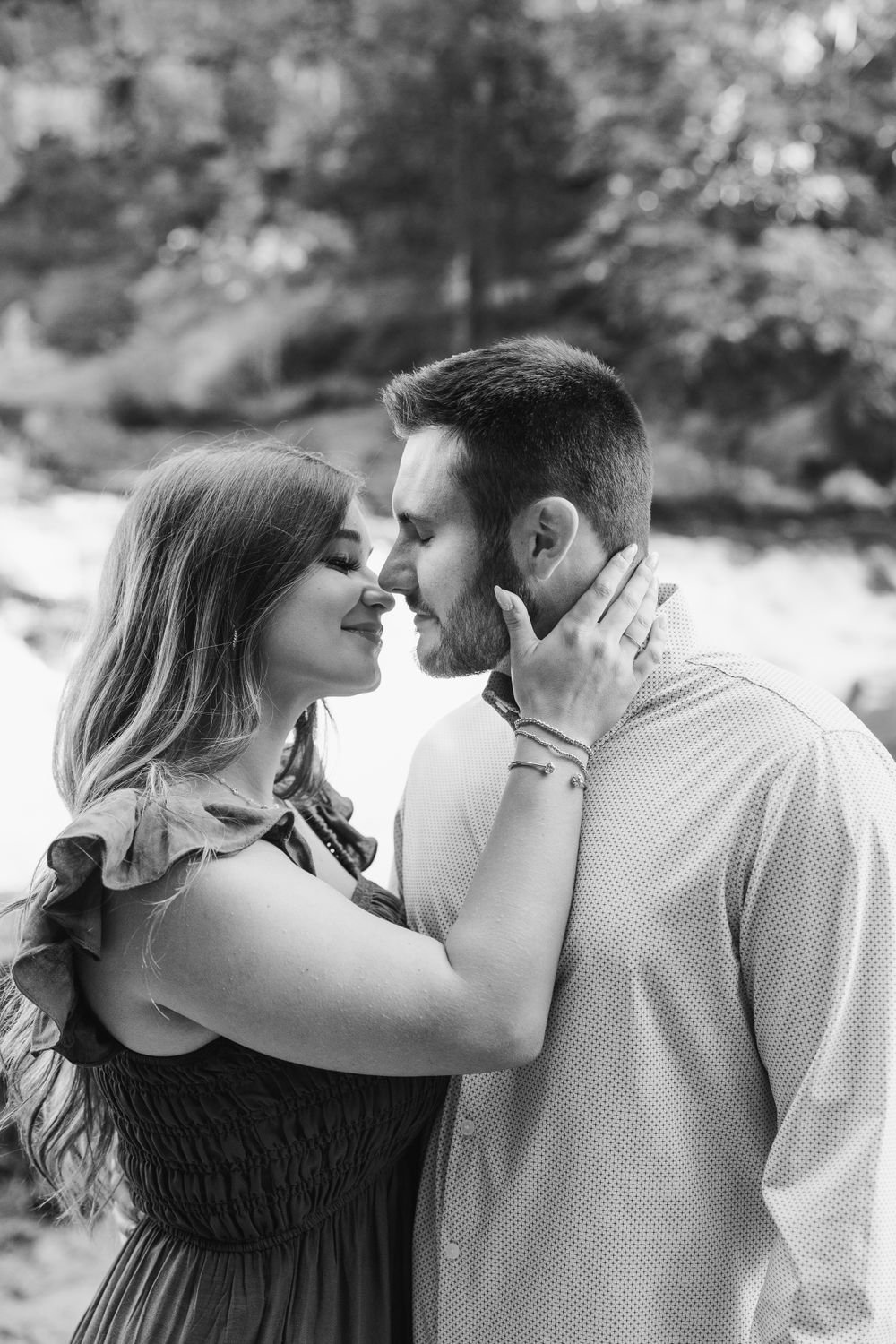 Romantic couple embracing in black and white portrait against natural outdoor backdrop.