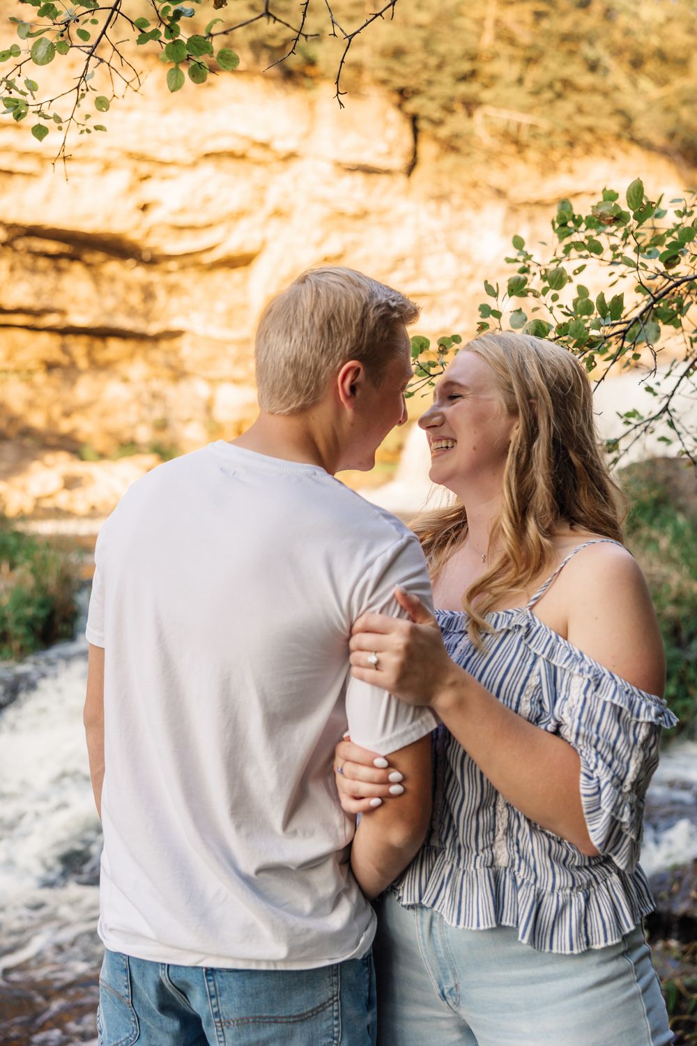 Couple sharing romantic moment against golden cliff face and waterfall backdrop.