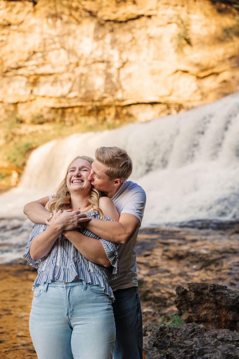 Joyful couple embracing by waterfall during outdoor photoshoot.