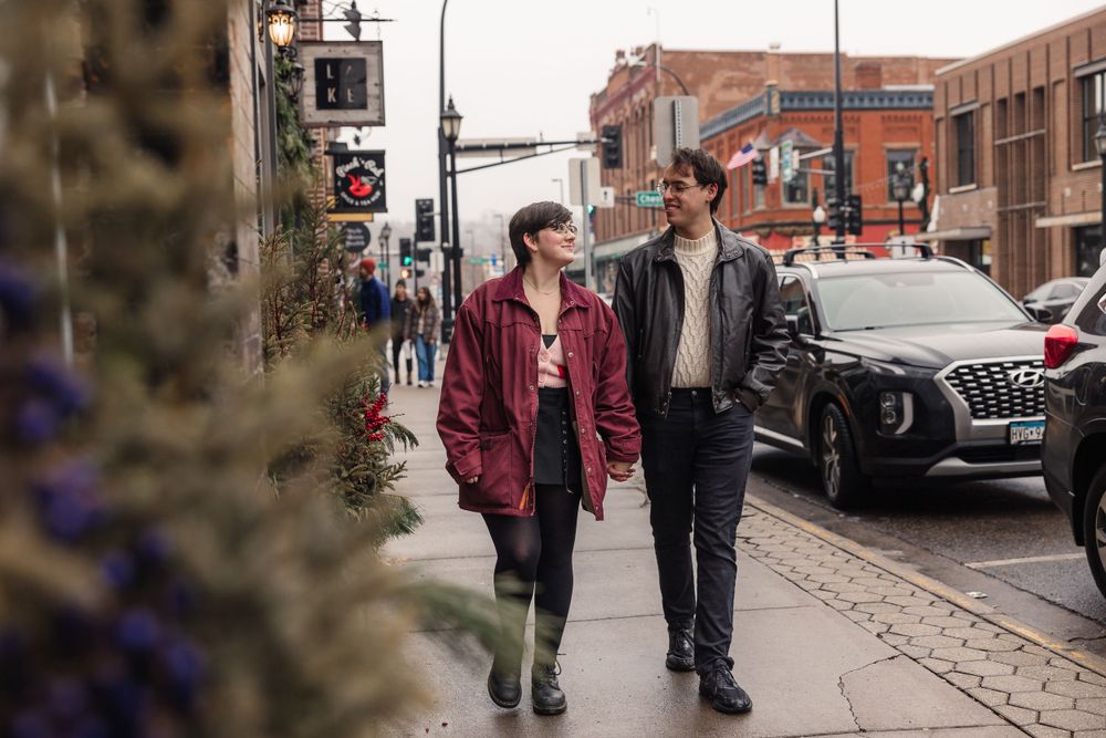 Couple walking together through an urban setting with brick buildings and streets.