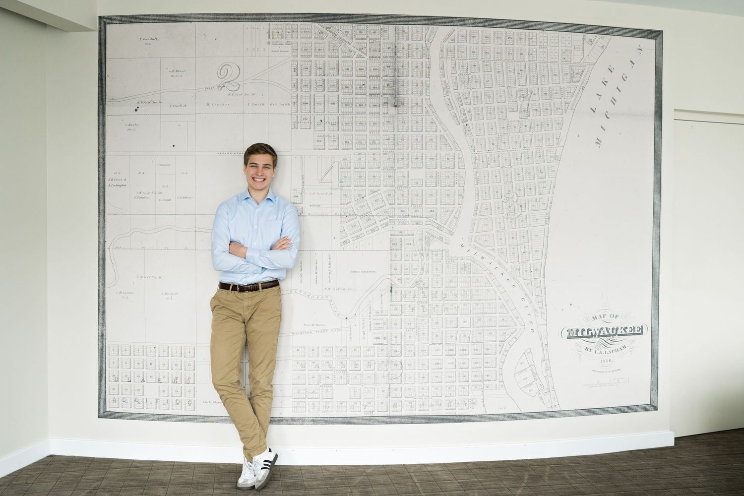 Smiling entrepreneur leaning against white wall with arms crossed - shot by Milwaukee professional headshot photographer Rachel Dickman.