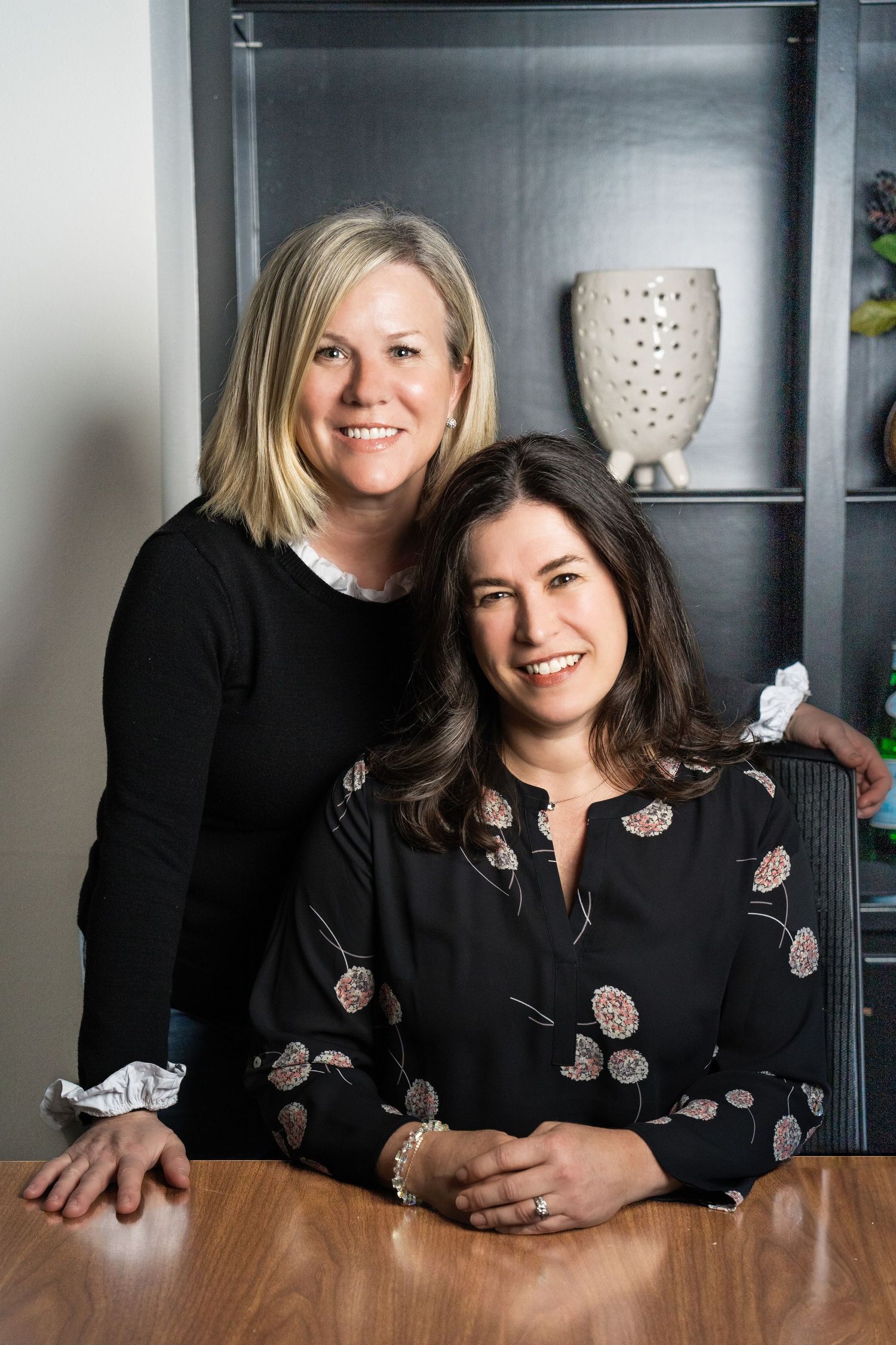 2 businesswomen seated at table smiling - professional corporate headshot by Rachel Dickman