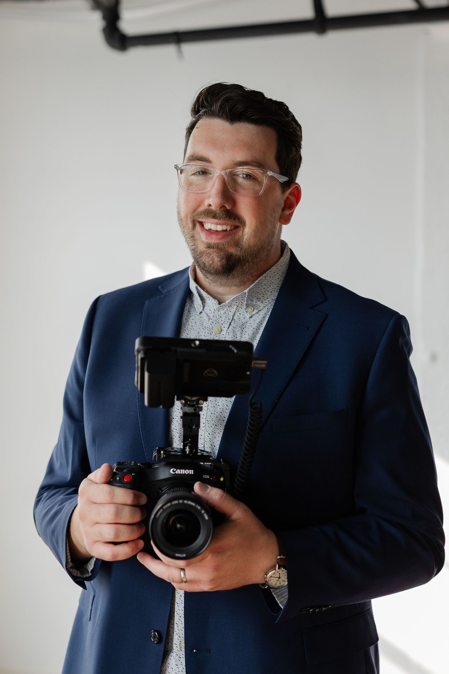 Professional photographer holds camera equipment while posing on a rooftop during golden hour.
