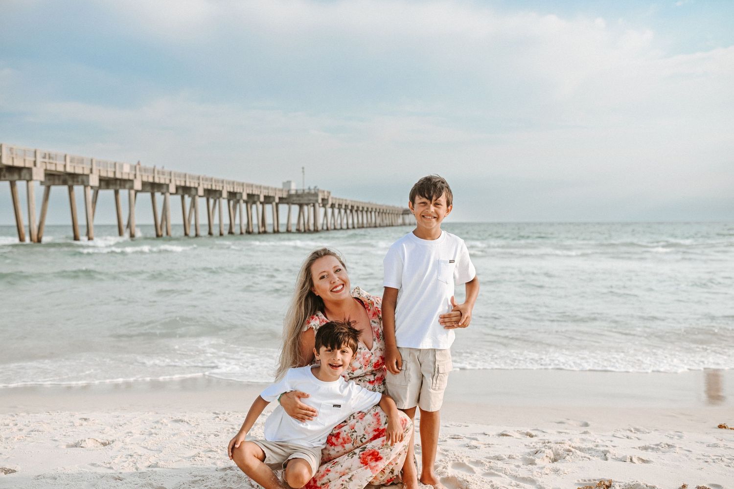 Happy family enjoying quality time together on sunny beach with pier in background.