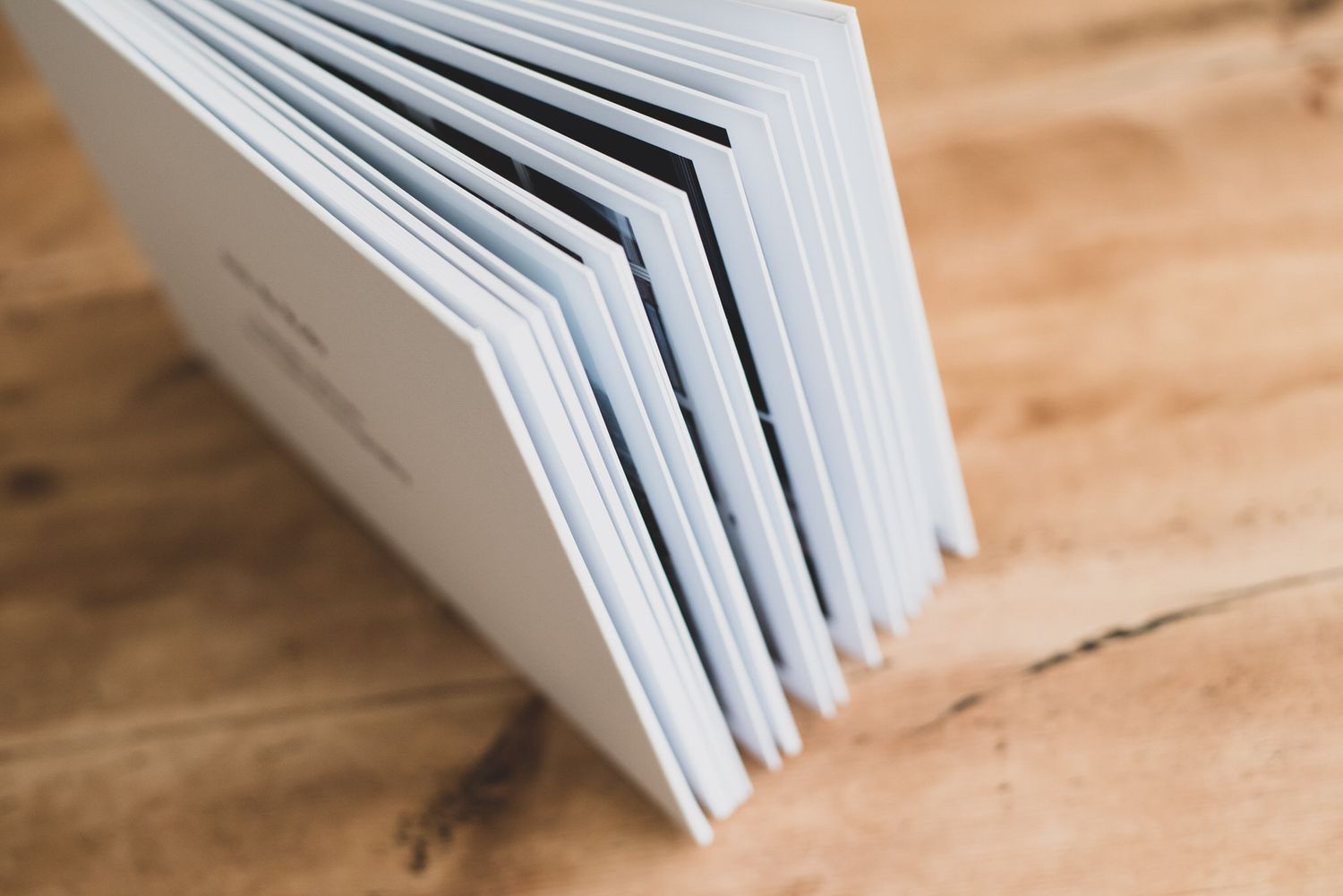Close-up of an open white hardcover book standing upright on a wooden table, showing layered pages.