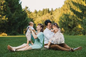 Family members lie together on grass in matching outfits during golden hour sunset photography session.