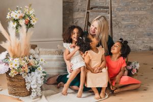 A mother and her three children laughing and having fun while lounging on floor with floral arrangements and decor.