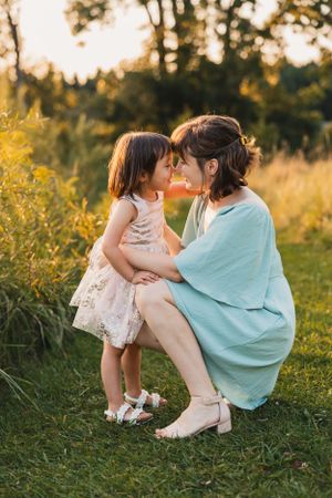 A tender moment shared between parent and child in a sunlit meadow wearing matching white and turquoise outfits.