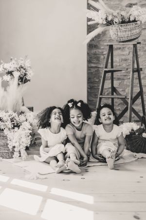 Three children sitting on floor laughing and playing together in a series of black and white lifestyle photographs.