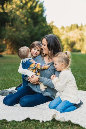 A family sits together on a white blanket outdoors sharing joyful moments in a grassy field during golden hour.