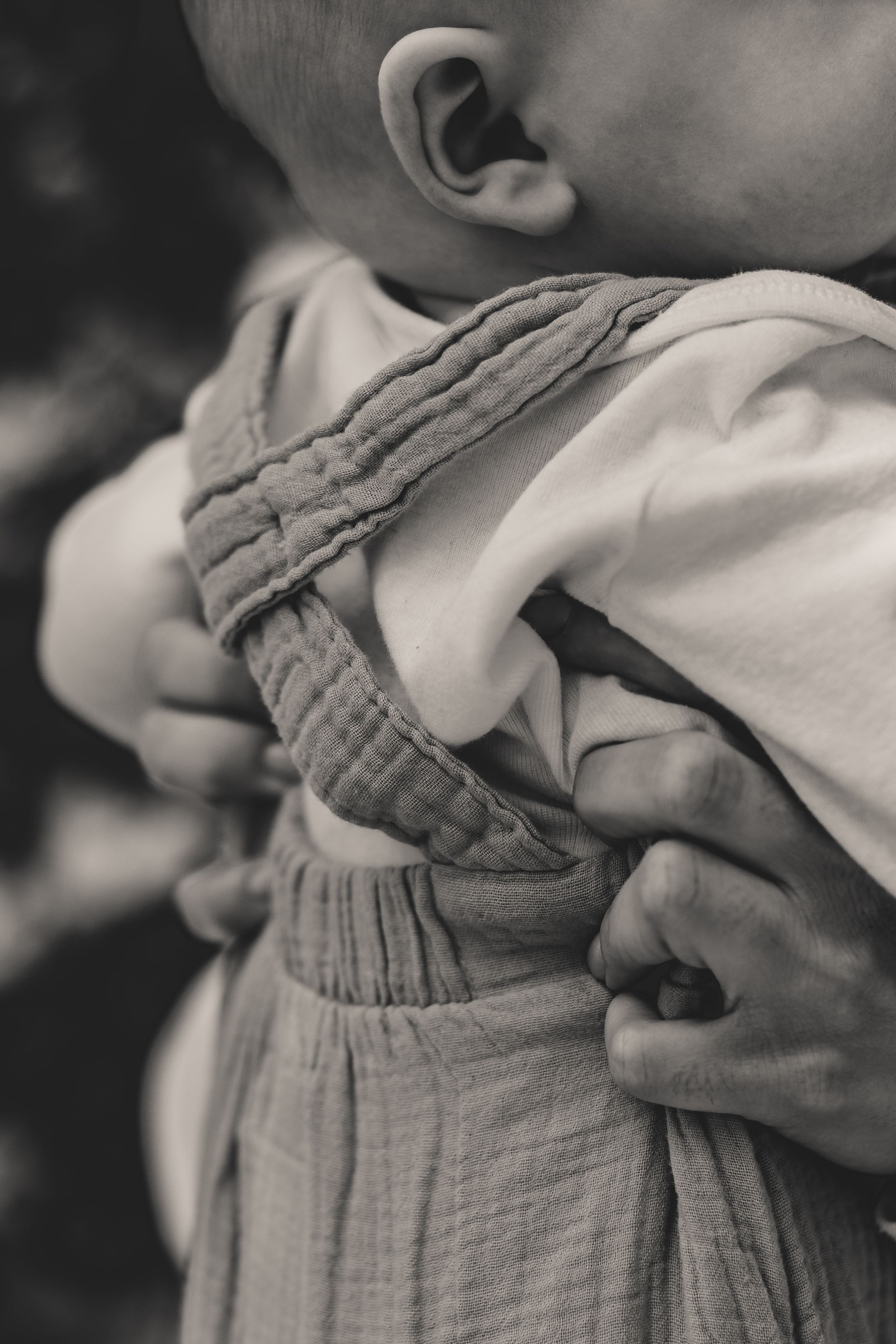 Close-up black and white photo showing a small child wearing a gathered cotton romper with ruffled details.