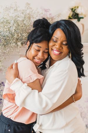 A mother and daughter embrace warmly and share joyful laughter in a light-filled studio setting.