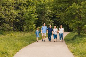 A group walks together on a paved trail through lush green summer woods on a sunny afternoon.