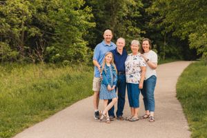 A couple and their children and grandchild walk together on a winding nature trail surrounded by lush green trees and foliage.