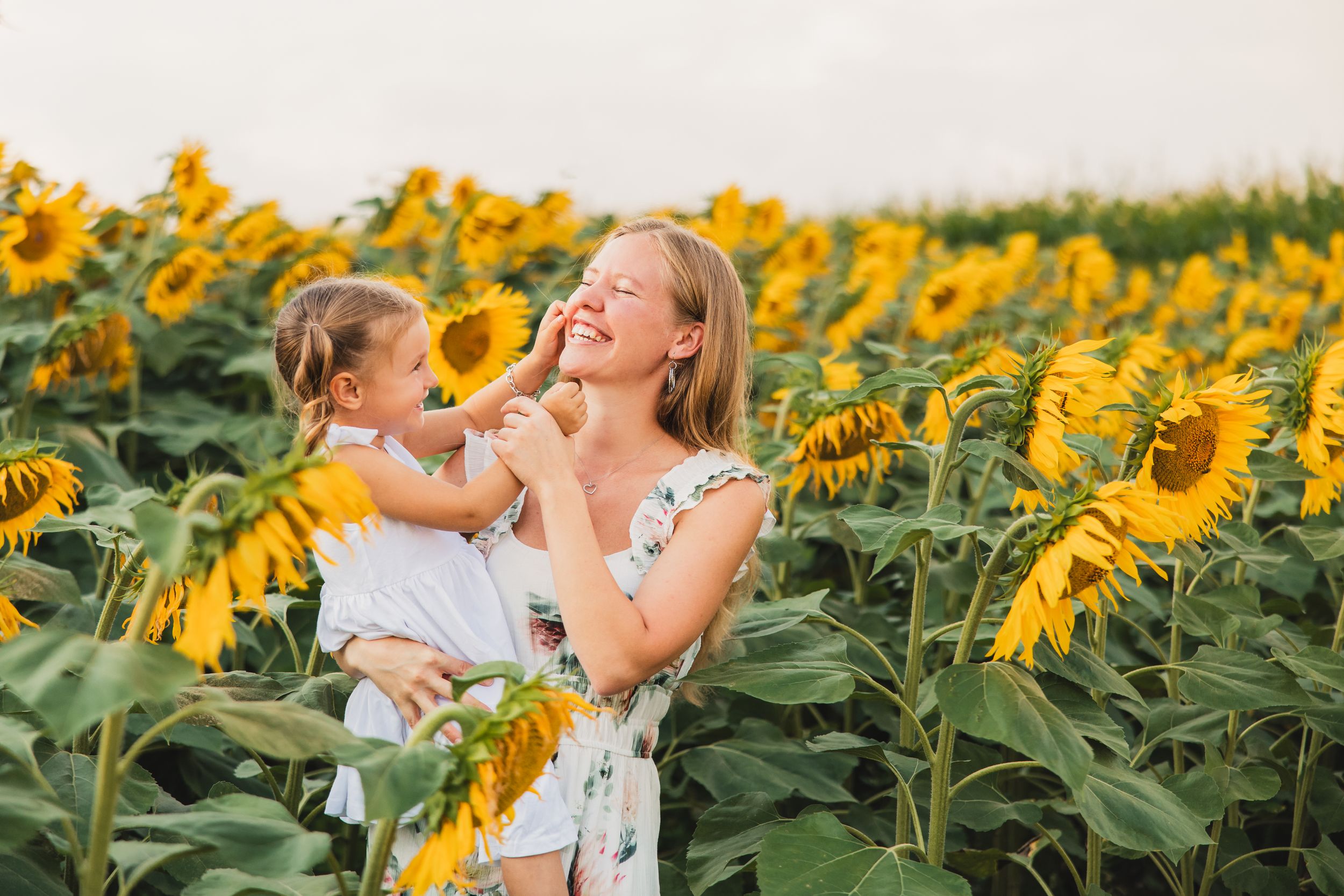 A joyful moment between a mother and daughter is captured in a vibrant sunflower field during golden hour.