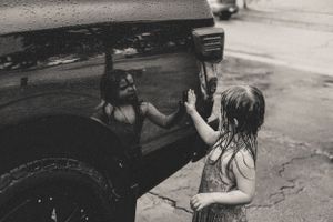 Black and white photo series shows a child playing in the warm summer rain and looking at her reflection.