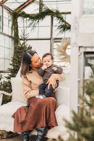 A parent and baby share tender moments while sitting together in a cozy greenhouse setting.